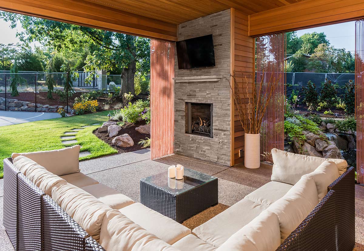 l-shaped couch around a coffee table under a covered patio with a nearby fireplace